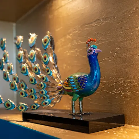 Gläserner Pfau als Wandschmuck in einer beleuchteten Nische